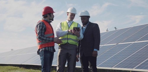 Eine Photovoltaikanlage auf einer Wiese mit drei Männern die auf ein Tablet schauen